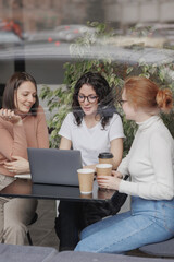 three female colleagues or students are working on a laptop and discussing a project or creative...