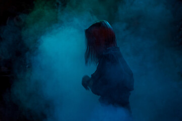 A girl with long hair in smoke in the spotlight. Low key. Soft focus