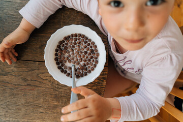 Caucasian preschool girl eating chocolate cereals with milk before school. Lifestyle morning...