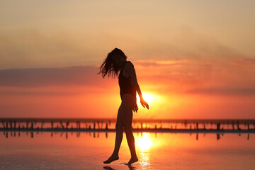 silhouette of a young slim woman in a swimsuit who dancing at sunset on the sea. summer holiday