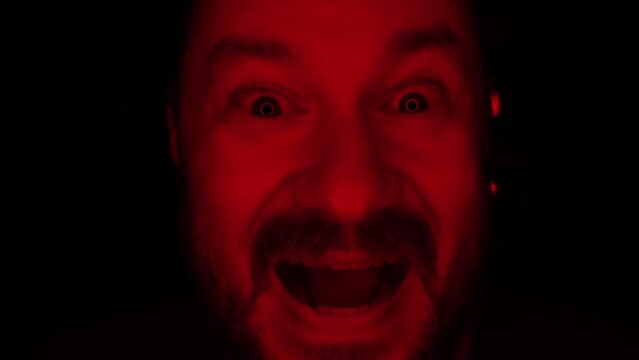 The evil laugh of an unshaven man illuminated by red light.