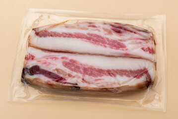 Italian Guanciale, slices dry cured pork cheek in in vacuum packed sealed for sous vide cooking isolated on light brown background