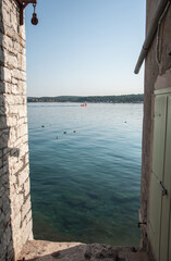 View of the Adriatic Sea and the town of Rovinj in Croatia from one of the many narrow streets in the city and a red excursion bathyscaph in the distance, early morning.