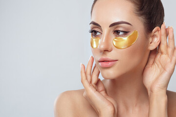 Beauty model girl face with healthy fresh skin. Woman with under eye collagen gold pads.  Skin care concept, anti-aging moisturizing eye mask, golden hydrogel patches, eye skin treatment, cosmetology