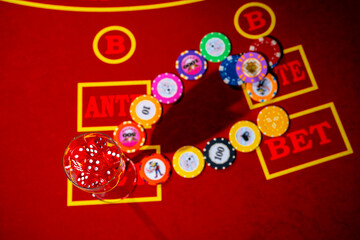 Top view of casino chips and a glass filled with red dice. A set of dice and playing chips for craps, poker, roulette on a red gaming table in a casino. Close up. Background of gambling.