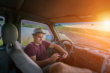 Tired driver wearing hat resting after work inside of truck cabin with digital tablet in hands