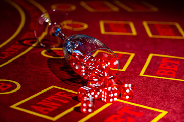 A fallen glass of champagne with red dice scattered across the table. Close up of a set of dice for craps, roulette, poker on a red gaming table in a casino. Gambling background.