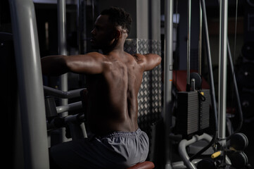 Naklejka na ściany i meble Shirtless african american man doing back exercises on a machine in the gym.