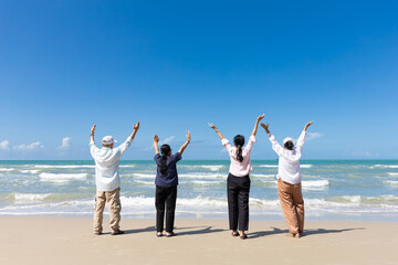 portrait back view group of seniors man and women with arms raised on the beach