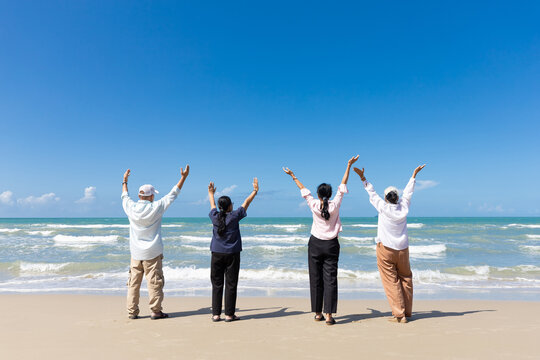 portrait back view group of seniors man and women with arms raised on the beach