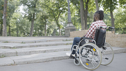 African-American man in wheelchair stopping near stairs, facing accessibility problem in the city