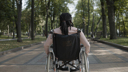 Obraz premium Back view of African American woman with disability riding wheelchair along park, resting outdoor