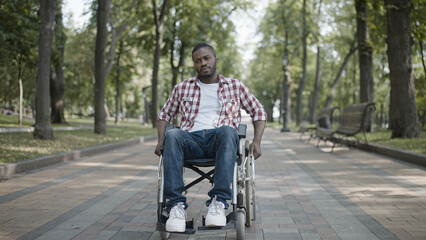 Serious black man with disability moving in manual wheelchair, rehabilitation