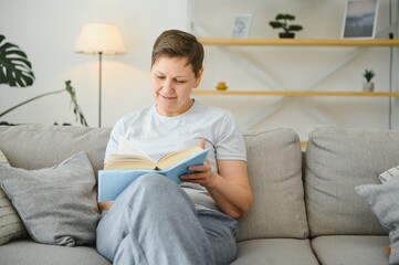 Attractive middle-aged woman with a lovely smile sitting on a sofa in the living room clutching a book.