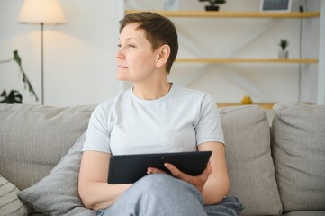 people, technology and internet concept - happy middle aged woman with tablet pc computer at home.