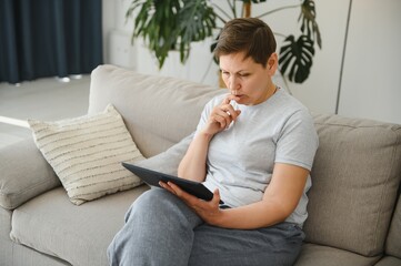 Obraz premium people, technology and internet concept - happy middle aged woman with tablet pc computer at home.
