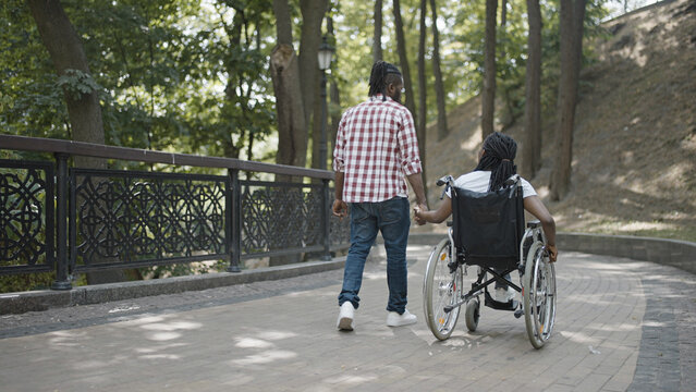 Loving husband holding hands with wife in wheelchair, couple walking in park, disability, togetherness