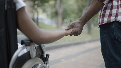 Man and woman in wheelchair holding hands, support in a relationship, love, close-up