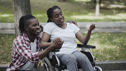 Young man and woman in wheelchair holding hands, talking, enjoying date in park