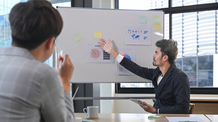 Male manager presenting project research results to interns colleagues, business partners team at meeting