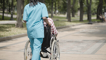 Back view of nurse pushing male patient in wheelchair, recovery after surgery - obrazy, fototapety, plakaty