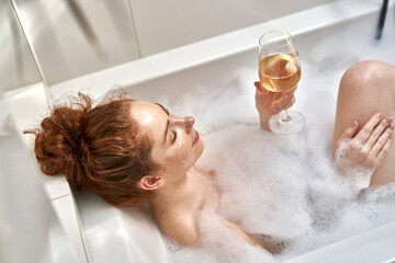 Caucasian redhead woman taking a bath and drinking wine