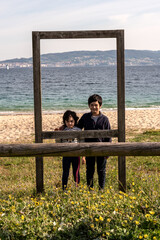 portrait a boy and a girl behind a wooden frame on the beach