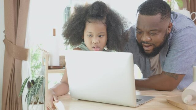 African America father and daughter learning recipe cooking online on laptop computer for cooking bakery or bread at home, dad and child preparing food, domestic life, family and lifestyles concept.