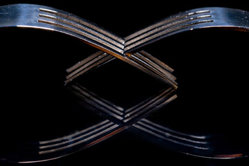 Two interlocking forks reflecting off a glossy black surface. Silver cutlery close up. Silverware,...