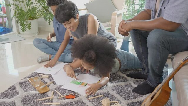 Happiness family with father and mother looking children drawing with colorful pencils and encouragement together in the living room at home, activity and hobby for learning, education concept.