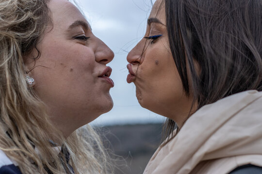 A lesbian couple kissing each other with puckering lips at night in the outdoors