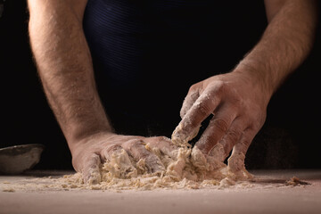 Cooking, kneading dough. Male hands mix the ingredients for the dough on the table against a dark background.