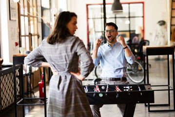 Colleagues having fun at work. Businessman and businesswoman playing table soccer.