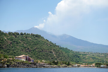 Vista panoramica del vulcano Etna, durante un'eruzione con colata lavica, fotografato dalla barca a mare, con la collina di Santa Tecla in primo piano - obrazy, fototapety, plakaty