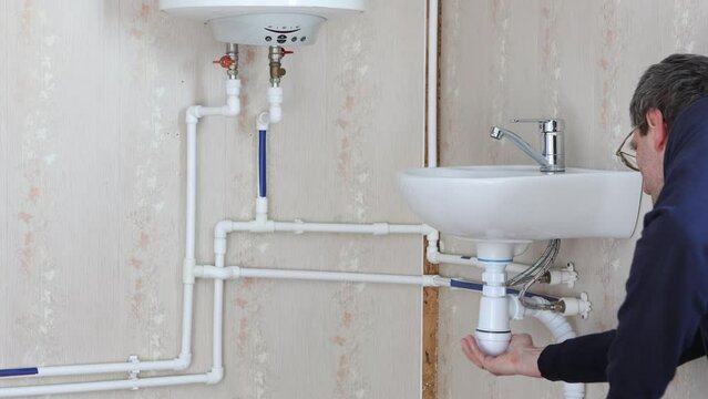 Cleaning of siphon under sink in bathroom, plumber is twisting cap.