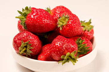 Lots of red juicy strawberries in a white plate on a white background, side view close-up