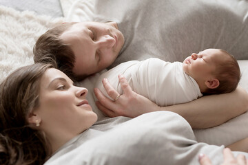 Newborn baby in mother's and father's arms on bed. Postcard Mother's and father's day. Children Protection Day. World Happiness Day. Smiling child. Happy parenthood
