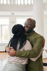Young smiling black man giving hug to worried or unhappy African American woman while comforting...