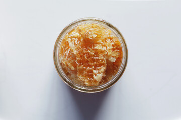 Top view open glass jar filled with fresh honey in beeswax placed on white table