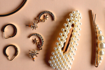 Various gold jewelry and pearl hair clips on peach colored background. Flat lay.
