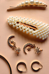 Various gold jewelry and pearl hair clips on peach colored background. Flat lay.