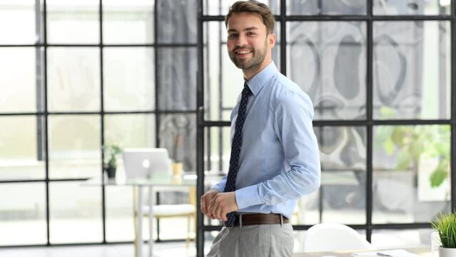 Smiling young happy businessman looking at camera standing at office