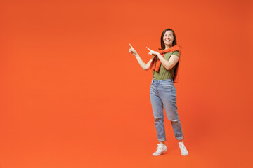 Full body young happy woman in khaki t-shirt tied sweater on shoulders point index finger aside on workpace area mock up isolated on plain orange background studio portrait. People lifestyle concept.