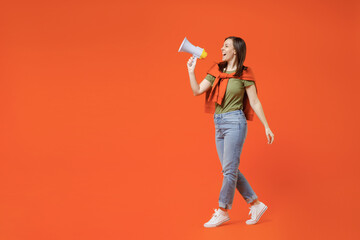 Full body side view young happy woman 20s wear khaki t-shirt tied sweater on shoulders hold scream in megaphone announces discounts sale Hurry up isolated on plain orange background studio portrait