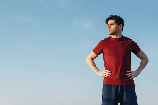 Bottom view young strong sporty athletic toned fit sportsman man 20s wear sports clothes stand akimbo look aside warm up training at sunrise sun dawn over sea beach outdoor on pier seaside in morning.