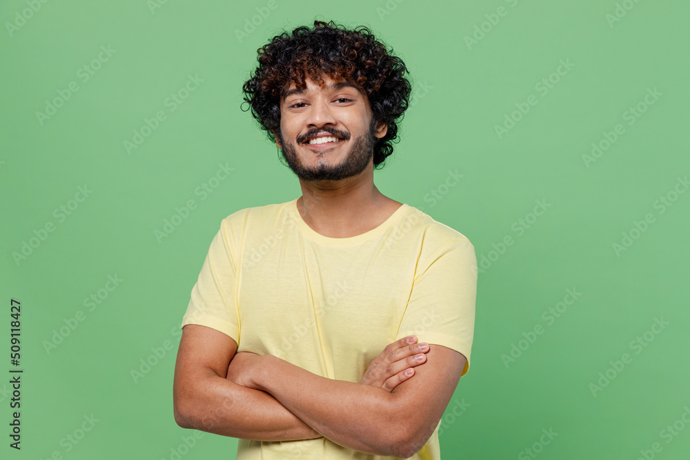 Wall mural Young smiling confident happy Indian man 20s in basic yellow t-shirt hold hands crossed folded look camera isolated on plain pastel light green background studio portrait. People lifestyle concept - Wall murals