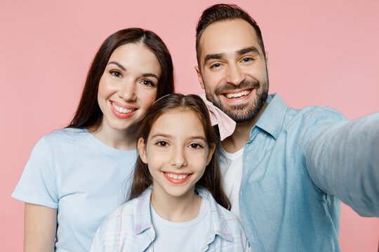 Close up young happy parents mom dad with child kid daughter teen girl in blue clothes doing selfie shot pov on mobile cell phone isolated on plain pastel light pink background. Family day concept