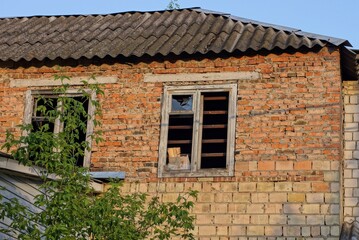 brown bricks attic of an old house with a broken window on the street against a background of blue sky 