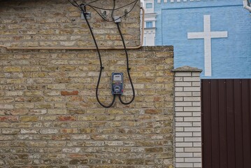 one gray electric meter with black wires on a brown brick wall of a building on the street