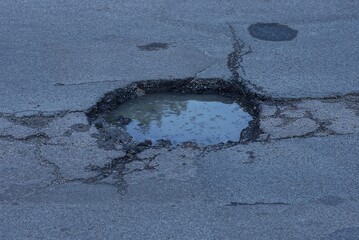 one pit pothole with dirty water on the gray asphalt road on the street